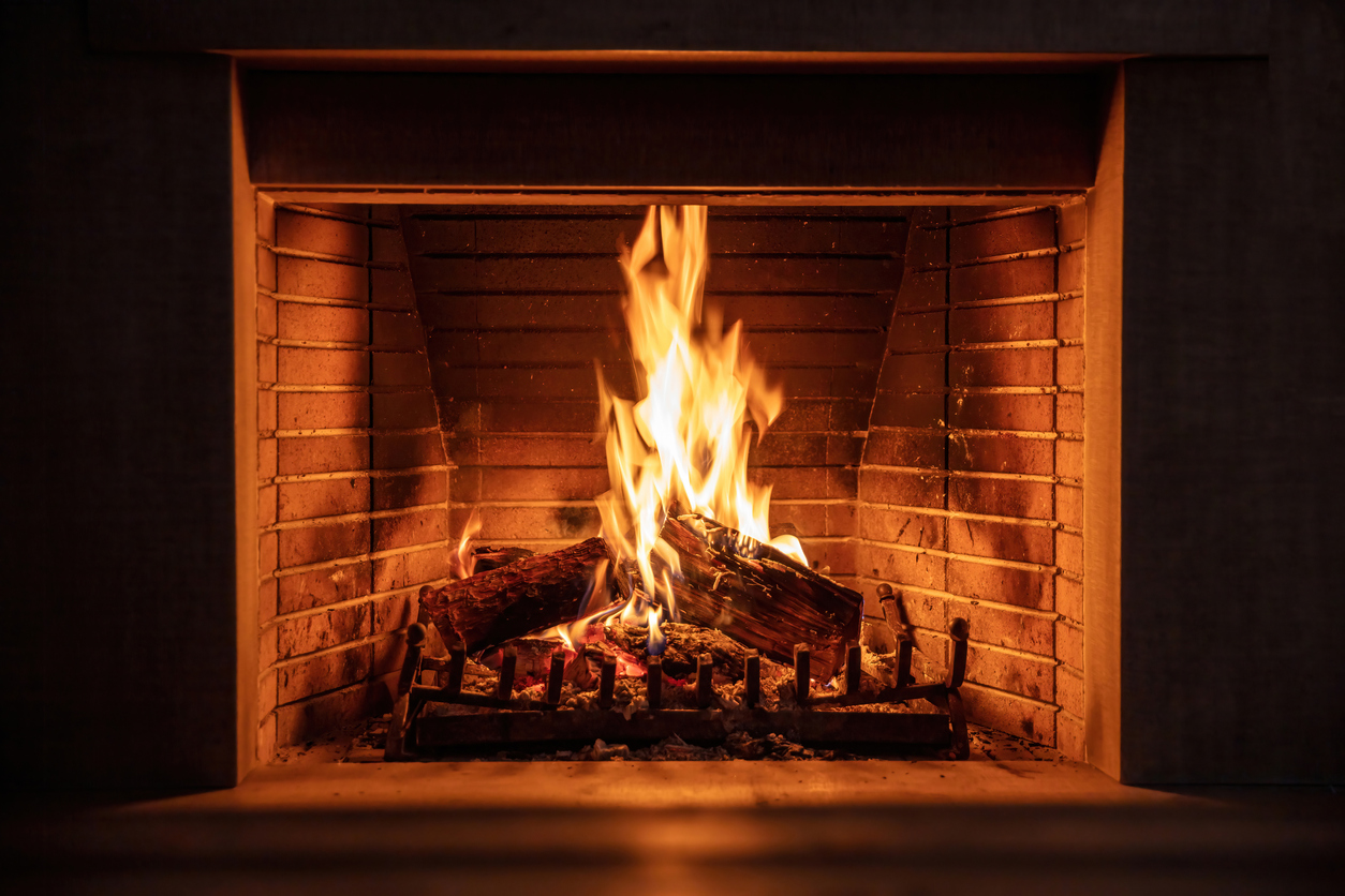 Fireplace burning firewood, fire flames on wood logs, bricks background. Cozy warm home
